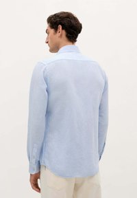 Camicia a maniche lunghe azzurro chiaro con colletto classico, polsini con bottoni e un orlo leggermente curvato. Realizzata in tessuto leggero e testurizzato.