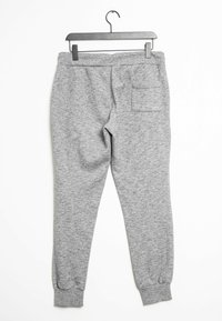 Szare dresowe spodnie z dzianiny z elastycznymi ściągaczami i jedną tylną kieszenią, wiszące na czarnym wieszaku na białym tle.