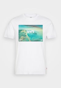 Camiseta de algodón blanca con un gran estampado gráfico colorido de un paisaje costero y el texto 'Levi's Worldwide' en el centro. Mangas cortas.