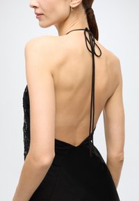 Black dress with a low back and halter neckline. Features a fitted bodice with sequin detailing and smooth fabric. Ties at the back.