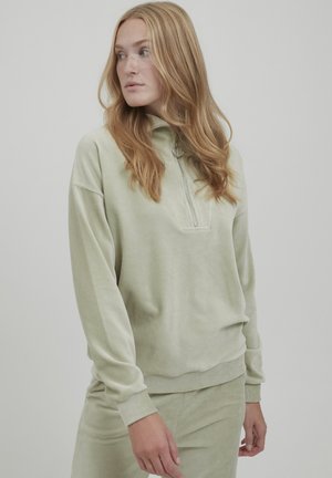 Pullover zip-up verde chiaro in morbido tessuto texturizzato con maniche lunghe. Presenta un piccolo colletto e dettagli di cucitura a vista.