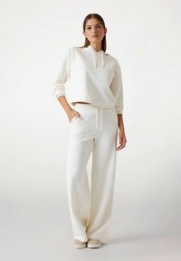 Completo da casa color crema composto da felpa cropped con coulisse e pantaloni a gamba larga, entrambi in tessuto morbido e testurizzato.