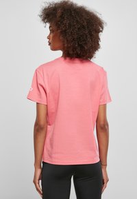 Tricou roz cu mânecă scurtă, cu decolteu rotund și o croială lejeră, având un logo cu stea pe mâneca stângă. Material din bumbac neted.