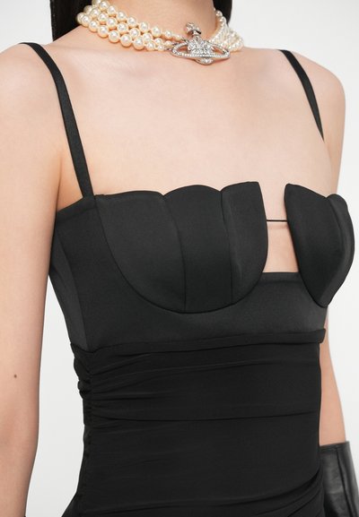 Vestito aderente nero con corpetto sagomato a onde, spalline sottili regolabili e dettagli arricciati in vita, abbinato a una collana di perle.