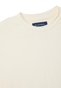 Crème-kleurig katoenen T-shirt met een ronde hals en korte mouwen. Heeft een marineblauw merklabel bij de kraag. Zachte textuur.