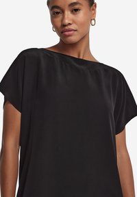 Sort løs pasform top med korte ærmer, der har en bred udskæring og glat, let skinnende stof. Minimalistisk design, ingen synlige mønstre.