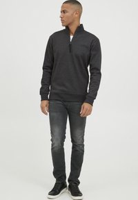 Pulover gri cu guler cu fermoar în material moale, având manșete și tiv din material elastic, asortat cu blugi negri și adidași negri. Design simplu, casual.