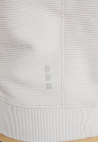 Gros plan d’un tissu côtelé gris clair avec une couture verticale et trois petits détails carrés réfléchissants près de la couture.