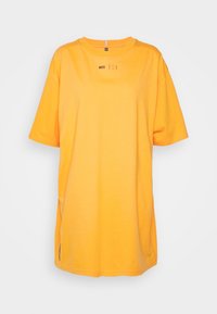 Žluté oversized tričko vyrobené z měkké látky, s krátkými rukávy, kulatým výstřihem a malým logem umístěným na přední straně.