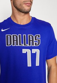 Royal blå Nike T-skjorte med "DALLAS" i fet sorte bokstaver og tallet "77" i strukturert grå, design med rund hals.