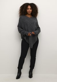 Poncho grigio lavorato a maglia con scollo a V, caratterizzato da motivi diagonali e maniche lunghe, abbinato a jeans skinny neri e stivali neri con tacco.