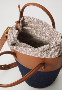 Brown leather bucket bag with a textured surface, denim lower section, and a patterned fabric lining in cream and burgundy. Adjustable strap included.