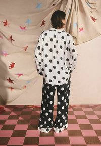 Čierna a biela blúzka s bodkami a široké nohavice, so voľným strihom, hladkou textúrou a kontrastnými vzormi na farebnom pozadí.