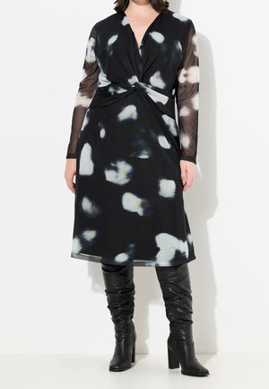 Czarna sukienka z przodem o skręconym designie, z przezroczystą, długą warstwą na rękawach oraz białymi abstrakcyjnymi wzorami. Połączona z czarnymi kozakami za kolano.