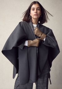 Poncho in lana grigio scuro con un design strutturato, dotato di un colletto grigio. Completato da guanti in pelle marrone chiaro e un abito grigio texturizzato.
