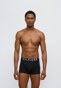 Μαύρα βαμβακερά μποξεράκια με μπλε σκούρο λάστιχο μέσης που φέρει λευκά γράμματα "HILFIGER". Λείο ύφασμα, εφαρμοστή σχεδίαση και μήκος μέχρι το μέσο μηρού.