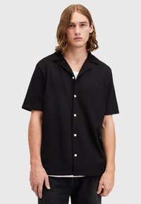 Short-sleeve black collared shirt made from smooth fabric, featuring white buttons and a subtle emblem on the chest.