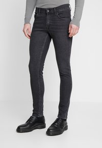 Pantalones vaqueros ajustados de color gris oscuro en tejido de dením, con cierre frontal de botón y cremallera, cinco bolsillos y un sutil desgastado.