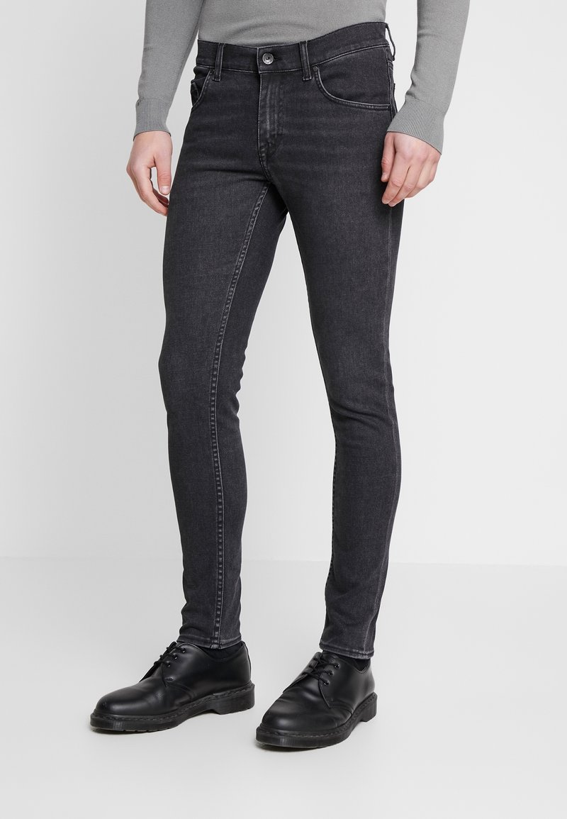 Pantalones vaqueros ajustados de color gris oscuro en tejido de dením, con cierre frontal de botón y cremallera, cinco bolsillos y un sutil desgastado.