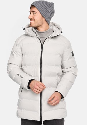 Puffy white jacket with a front zipper, hood, and black accents. Worn over a gray turtleneck, featuring a textured finish.