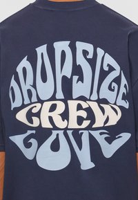 Marineblå crewneck t-shirt med stor, legesyg lyseblå og cremefarvet grafisk tekst: "DROPSIZE CREW LOVE" i varierende skrifttyper og former.