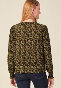 Blusa a maniche lunghe nera e verde oliva a motivo, con polsini arricciati e un design posteriore dritto. Tessuto testurizzato con leggere pence.