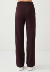 Pantalon ample couleur bordeaux foncé avec une taille élastique. Le tissu est lisse et doux, sans motifs visibles ni détails métalliques.