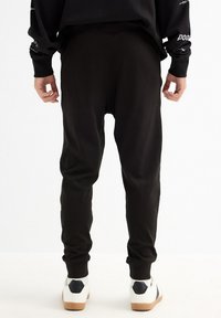 Pantalones de chándal negros hechos de tejido suave, con un ajuste holgado y puños acanalados. Combinados con zapatillas blancas con detalles en negro.