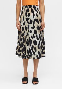 Jupe midi à imprimé léopard en beige et noir, avec un design évasé et une texture lisse. Associée à des sandales à glissière noires.
