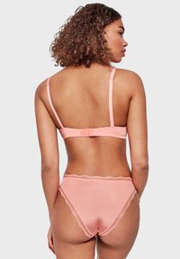 Set di reggiseno e bikini rosa chiaro, con spalline sottili, un bordo in pizzo sulla vita e una texture liscia. Visuale posteriore mostrata.
