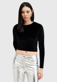 Fekete bársony, hosszú ujjú cropped top, fényes ezüstfém nadrággal párosítva. Figyelemre méltó textúrák közé tartozik a puha anyag és a tükröződő felület.
