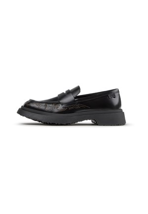 Musta nahkainen loafer, jossa paksu musta pohja, hienovarainen ruskea koristekuvio kärjen lähellä ja Camper-merkkinen lappu kannassa.
