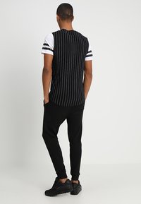 Black and white striped short-sleeve shirt with a solid white front, paired with black joggers and black athletic shoes.
