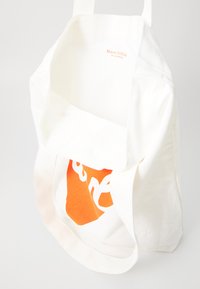 Hvit bomullstote med oransje grafisk design. Har robust stoff, skulderremmer, og synlig merkevaremerke innvendig.