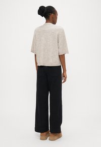 Beige, short-sleeve knit top with a relaxed fit, paired with black wide-leg trousers. Notable details include a crew neckline and minimal texture.