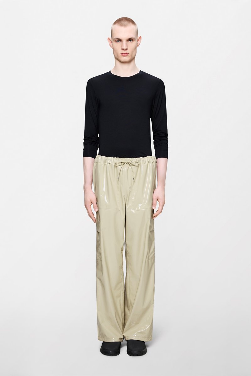 Μαύρο μακρυμάνικο πάνω μέρος συνδυασμένο με μπεζ γυαλιστερό παντελόνι cargo με κορδόνι στη μέση και πλαϊνές τσέπες, συνδυασμένο με μαύρα παπούτσια.