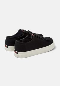 Sneakers neri in tela con punta tonda, suola in gomma bianca, lacci piatti e una piccola accentuazione rossa sul retro.