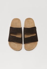 Sandale din suede maro cu un design plat, având două curele late și detalii decupate. Brânza interioară moale de nuanță bej cu accente de cusătură.
