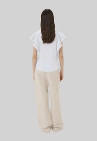 Top bianco a maniche corte con scollatura rotonda e maniche piegate, abbinato a pantaloni larghi in lino beige. Tessuto liscio, vestibilità rilassata.
