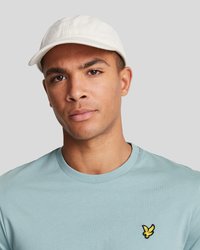 Casquette blanche avec un visière courbée, portée avec un t-shirt bleu clair présentant un petit logo noir et jaune sur la poitrine.