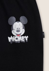 La tela negra presenta un gráfico caricaturesco de Mickey Mouse en blanco y gris, con la palabra "MICKEY" mostrada en una fuente llamativa y desgastada.