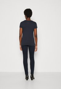 Marineblå t-skjorte med korte ermer kombinert med mørke skinny jeans og svarte ankelstøvler, med en tettsittende silhuett og glatt tekstur.