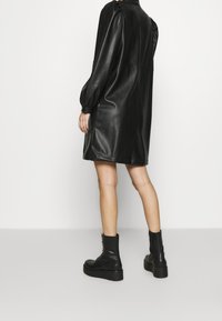 Robe en cuir noir à coupe décontractée, manches bouffantes et longueur aux genoux. Stylée avec des bottines noires à semelle épaisse.