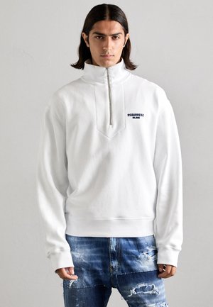 Weißer Pullover mit hohem Kragen, Reißverschluss und diamantförmigem Design auf der Brust. Mit einem Logo in Marineblau.