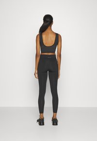 Zwart sportoutfit bestaande uit een aansluitend tanktop met een lage rug en hoog-wijde leggings. Beide stukken zijn glad en rekbaar van textuur.