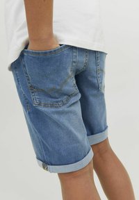 Pantalones cortos de mezclilla en azul claro con un aspecto ligeramente desgastado, que presentan dobladillos enrollados y dos bolsillos traseros con detalles de costura sutiles.