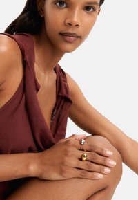 Dwa pierścionki na dłoni: jeden błyszcząca srebrna kula i jeden złoty owal, na tle, które podkreśla teksturę i kolor skóry.