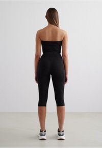 Black strapless top and black cropped leggings made of a stretchy fabric; paired with white and black athletic sneakers.