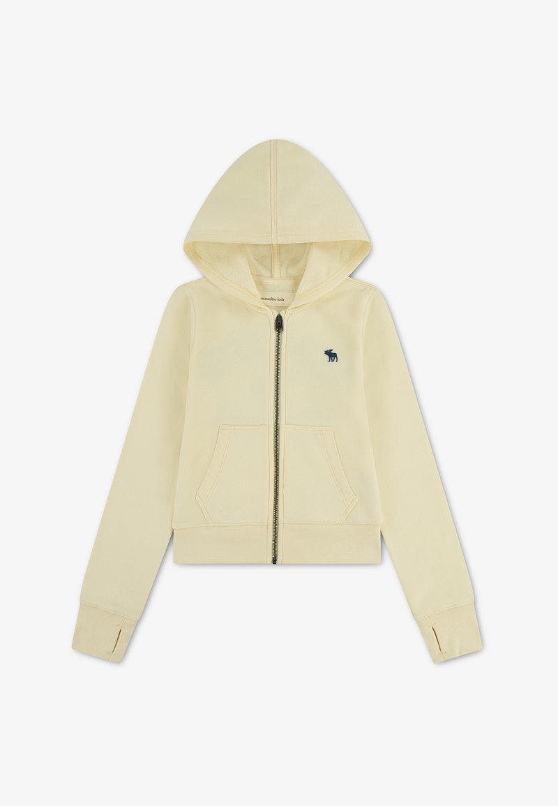 Sweat à capuche zippé enfant beige clair avec poches avant, trous pour les pouces aux poignets et petit logo élan bleu foncé sur la poitrine.