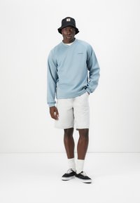 Light blue sweatshirt with long sleeves, gray denim shorts, black bucket hat, white socks, and black sneakers. Minimalist design with clean lines.